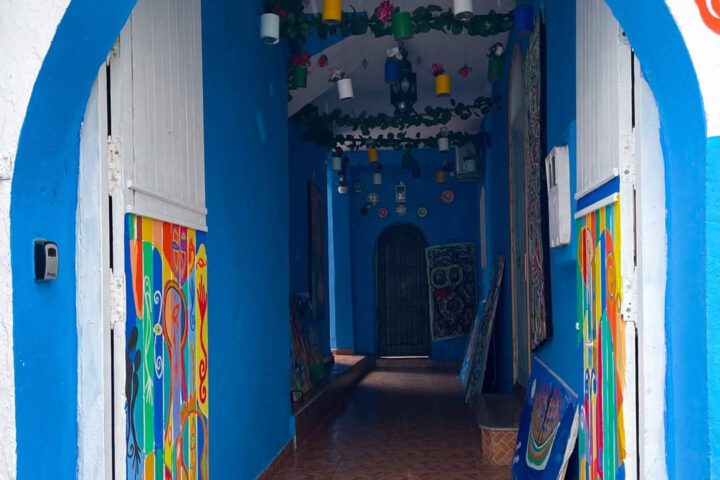 Colorful entrance to an art gallery in Asilah with blue walls, hanging plants, and vibrant paintings.