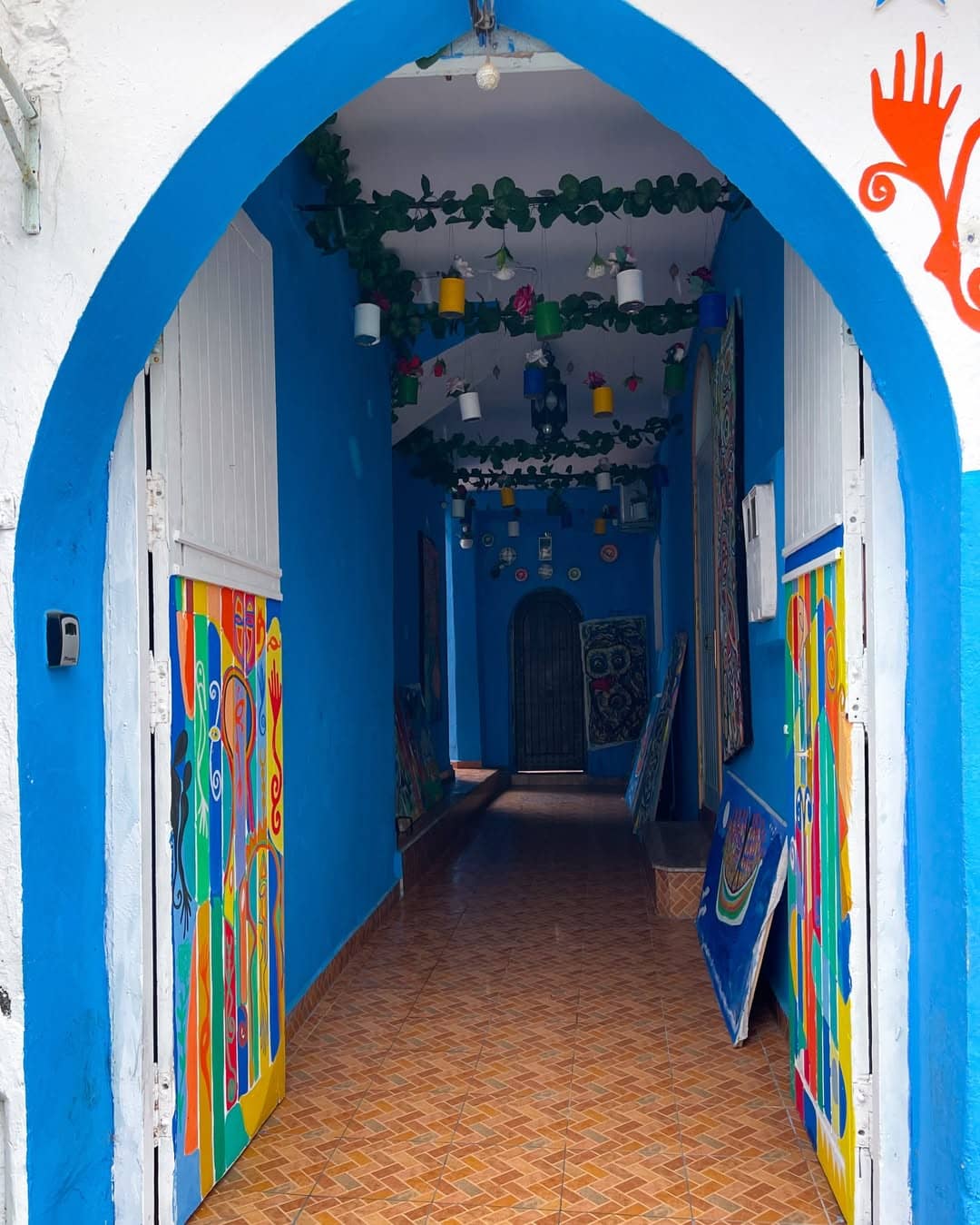 Colorful entrance to an art gallery in Asilah with blue walls, hanging plants, and vibrant paintings.