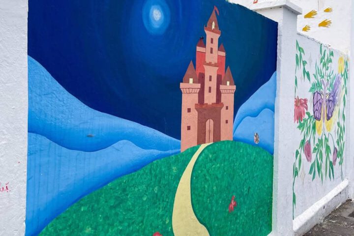 Colorful mural of a whimsical castle and handprints on a white wall in Asilah.
