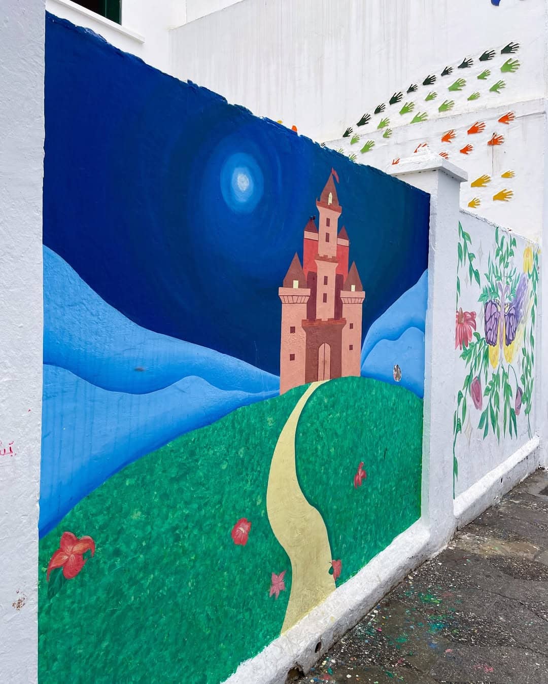 Colorful mural of a whimsical castle and handprints on a white wall in Asilah.