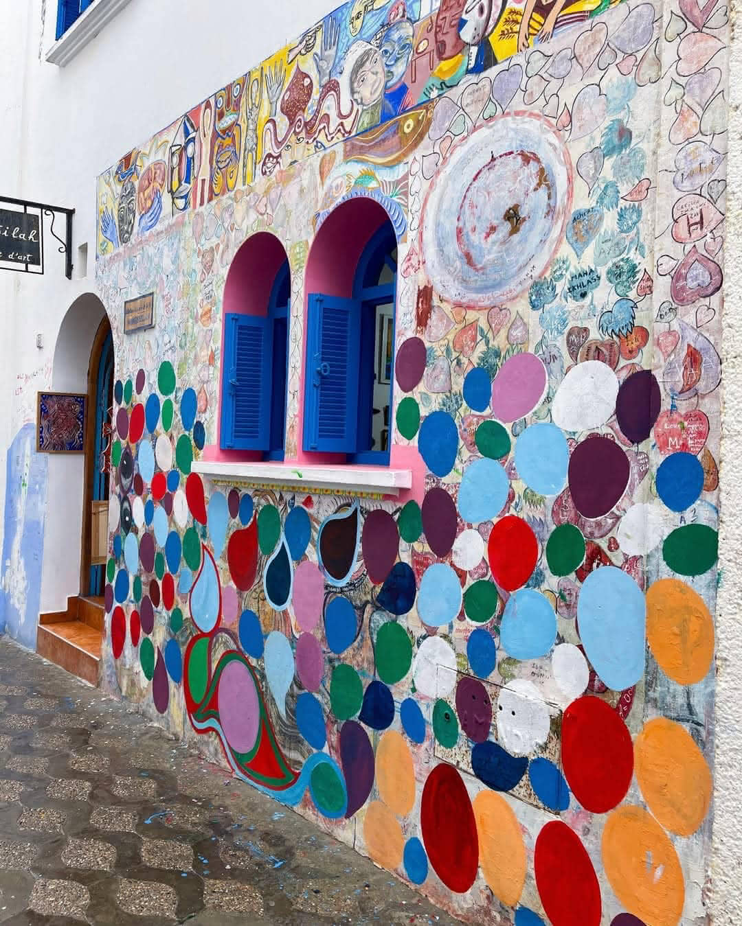 Vibrant mural with colorful circles, faces, and handwritten hearts on a creative wall in Asilah.