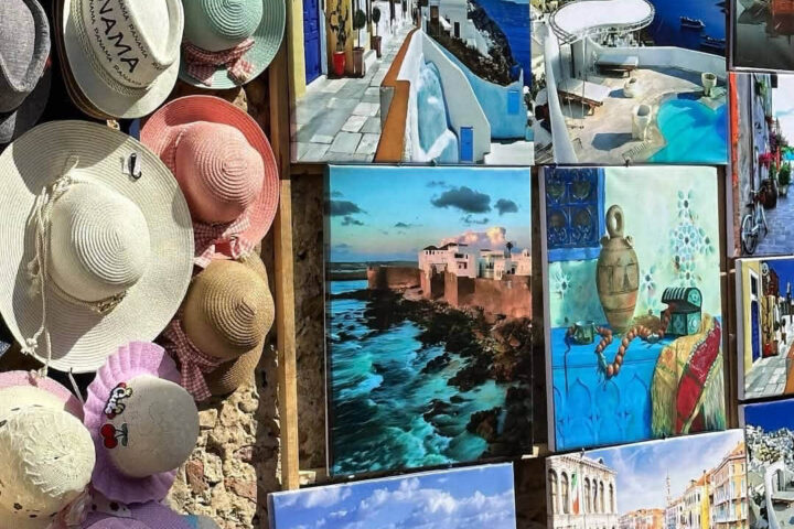 Display of handmade sun hats and colorful paintings in an Asilah street market on a Tangier day trip
