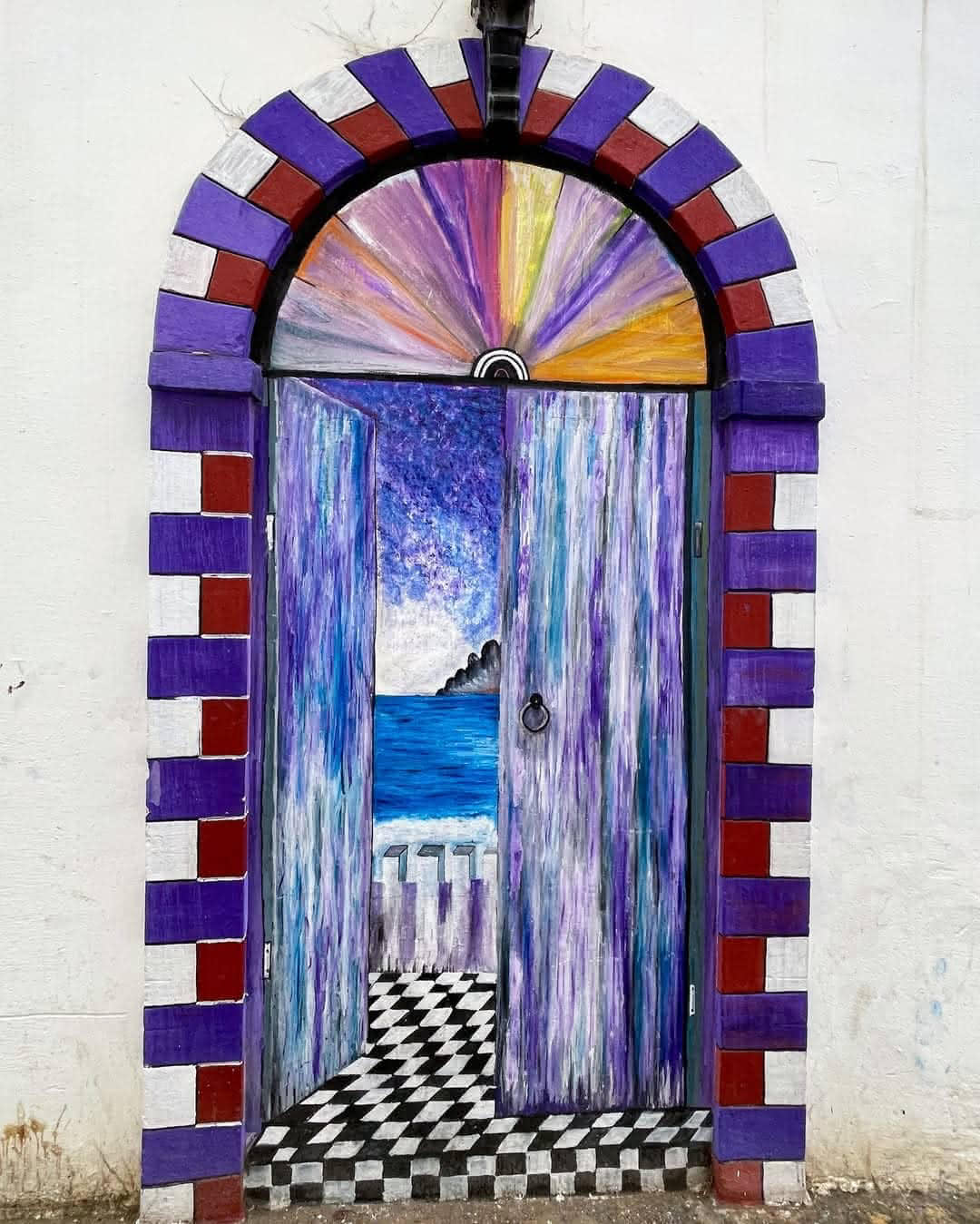Artistic mural of a painted doorway revealing an ocean view in Asilah’s medina.