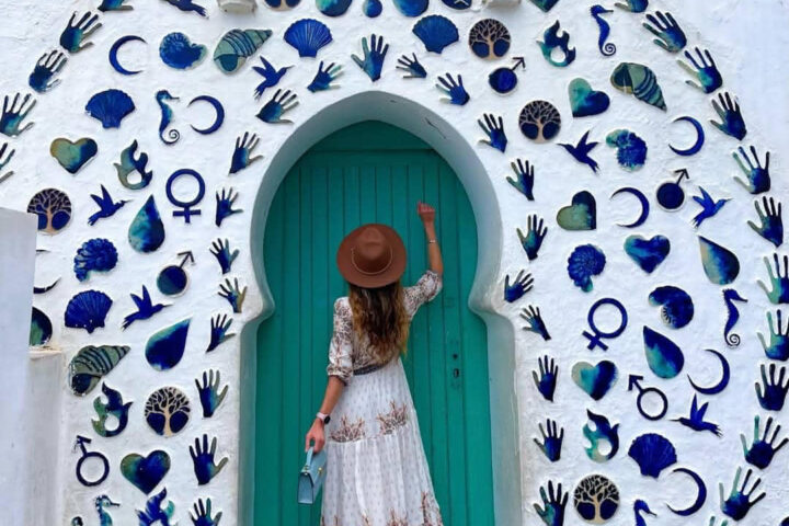 Traveler knocking on a turquoise arched door surrounded by a blue mosaic of symbols in Asilah.