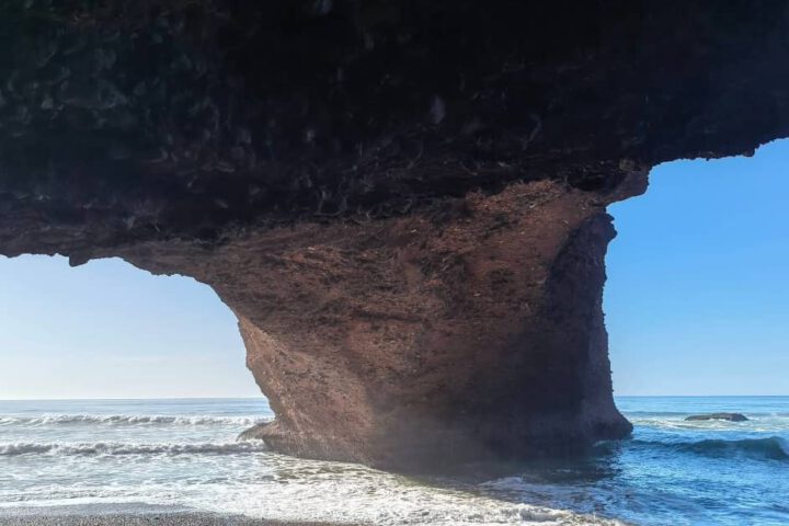 Walking beneath the large red arch at Legzira Beach near Agadir