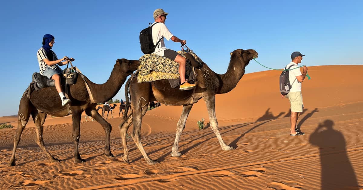 Family Camel Ride in Merzouga Desert with Local Guide Family riding camels across the Merzouga Desert in Morocco, guided by a local tour guide