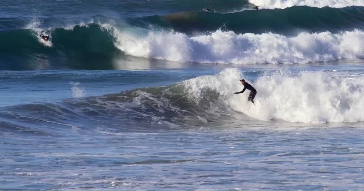 Surfer riding a wave near Taghazout on Morocco’s Atlantic coast under a clear winter sky.