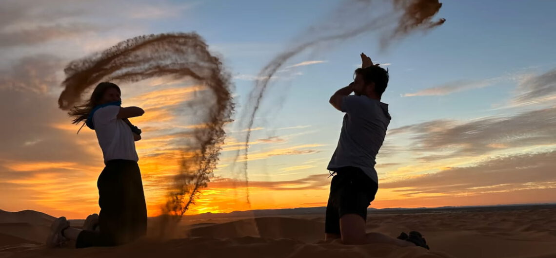 A couple playing with sand at sunset in the Erg Chebbi dunes during a Sahara desert tour.