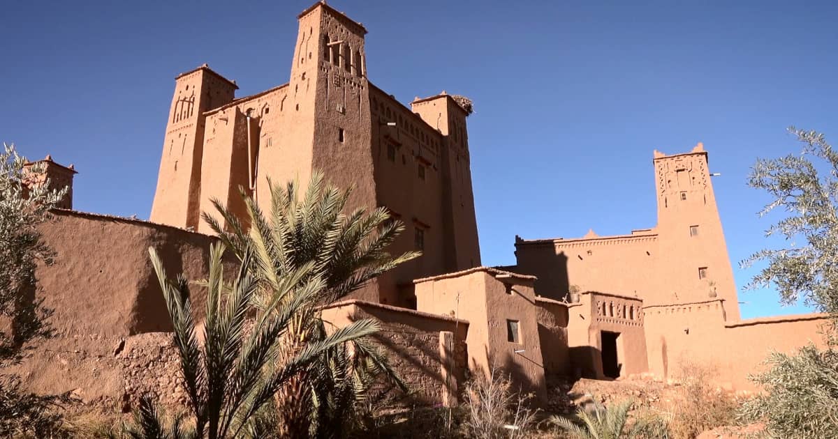 Kasbah of reddish clay with palm trees in a ounila valley.