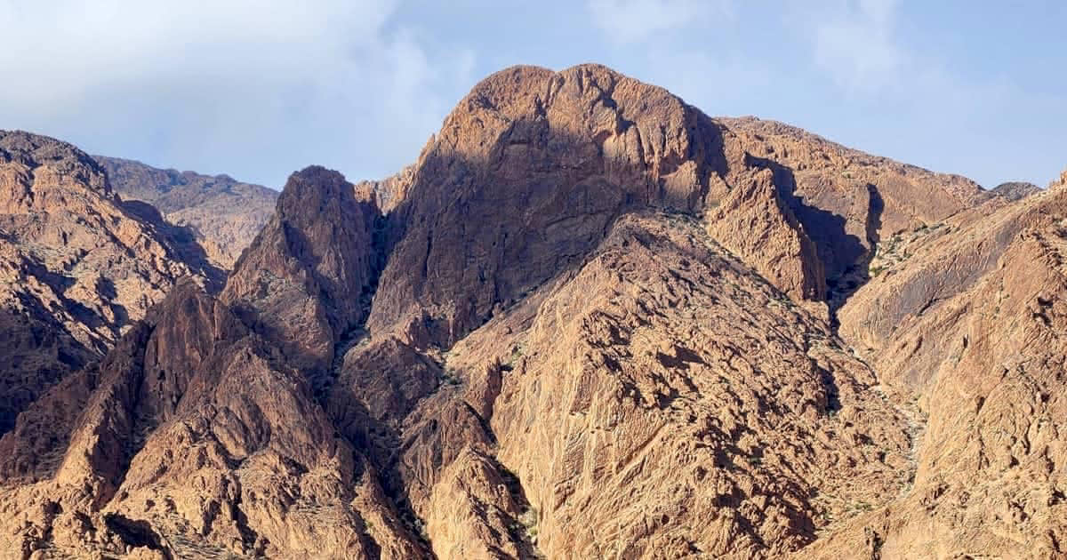 A wide shot of the rugged, sun-drenched granite peaks of Mount Lkest near Tafraout, Morocco, showing the natural 'Lion’s Face' rock formation.