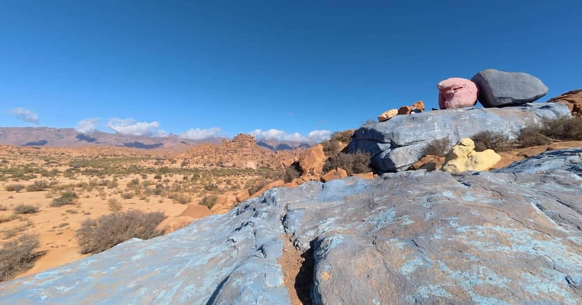 Large granite boulders painted in bright blue and pink under a clear sky in the desert landscape of Tafraout, Morocco