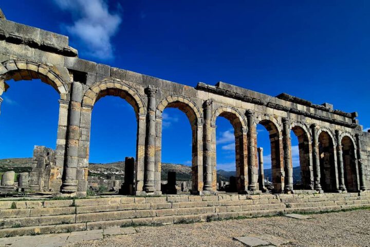Roman stone arches and columns at Volubilis with hills in the background.