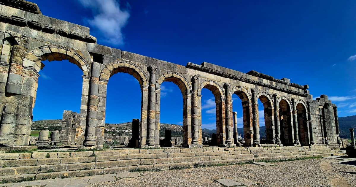 Roman stone arches and columns at Volubilis with hills in the background.