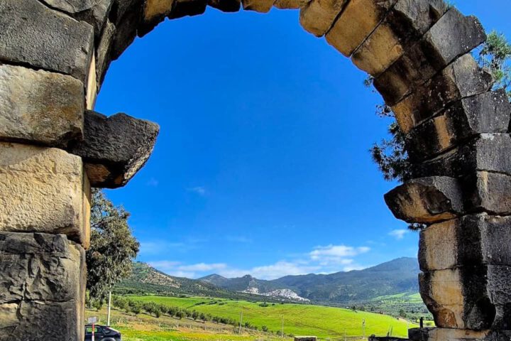 Ancient stone arch at Volubilis framing green fields and distant hills.