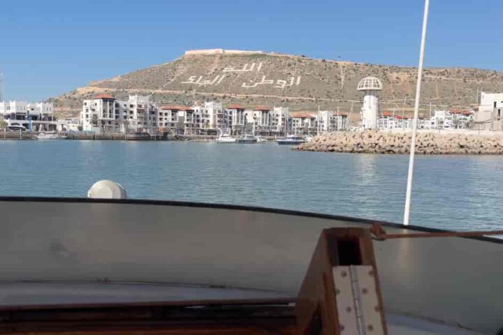 Blick auf die Marina von Agadir vom Boot mit Hügel und Schriftzug Agadir Oufella im Hintergrund