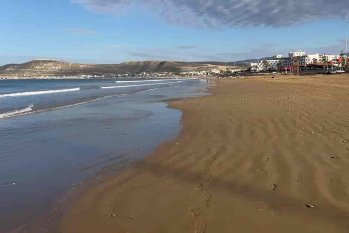 Weiter Sandstrand in Agadir mit sanften Wellen und Blick auf die Küstenlinie der Stadt